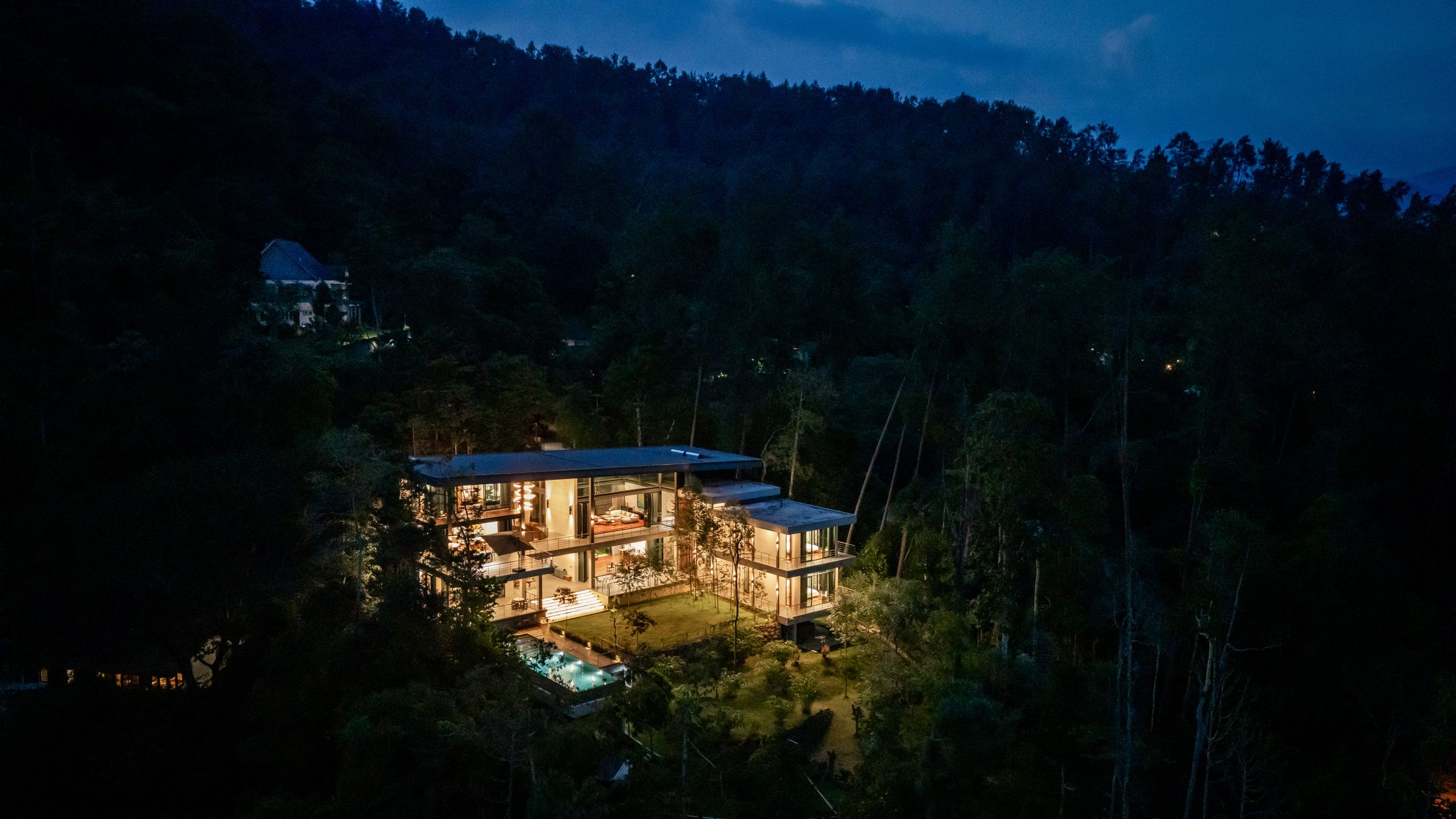 SereneNest private villa glowing in the rainforest at dusk, seen from a distance