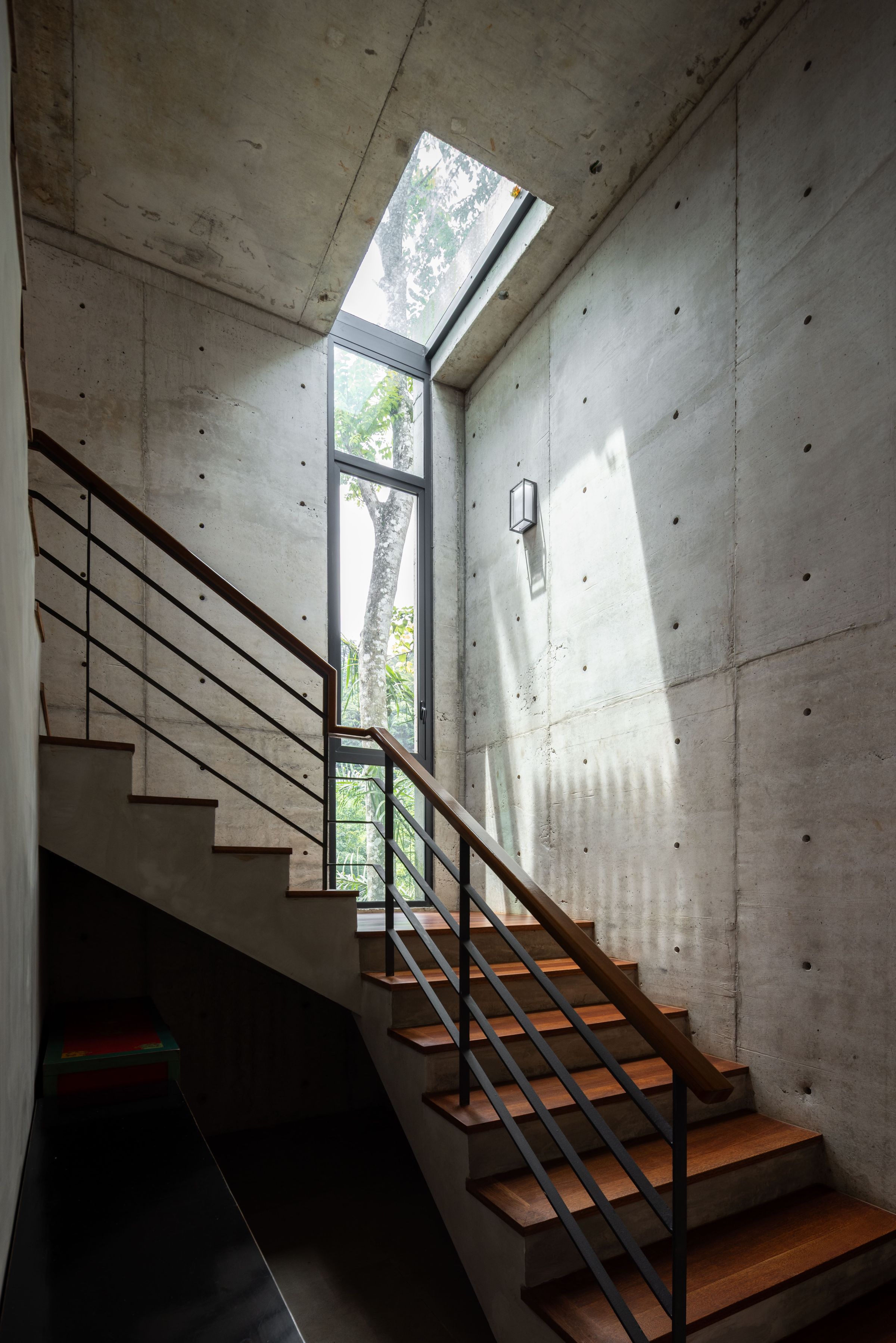 Raw concrete stairwell and corridor inside the SereneNest villa with slatted daylight