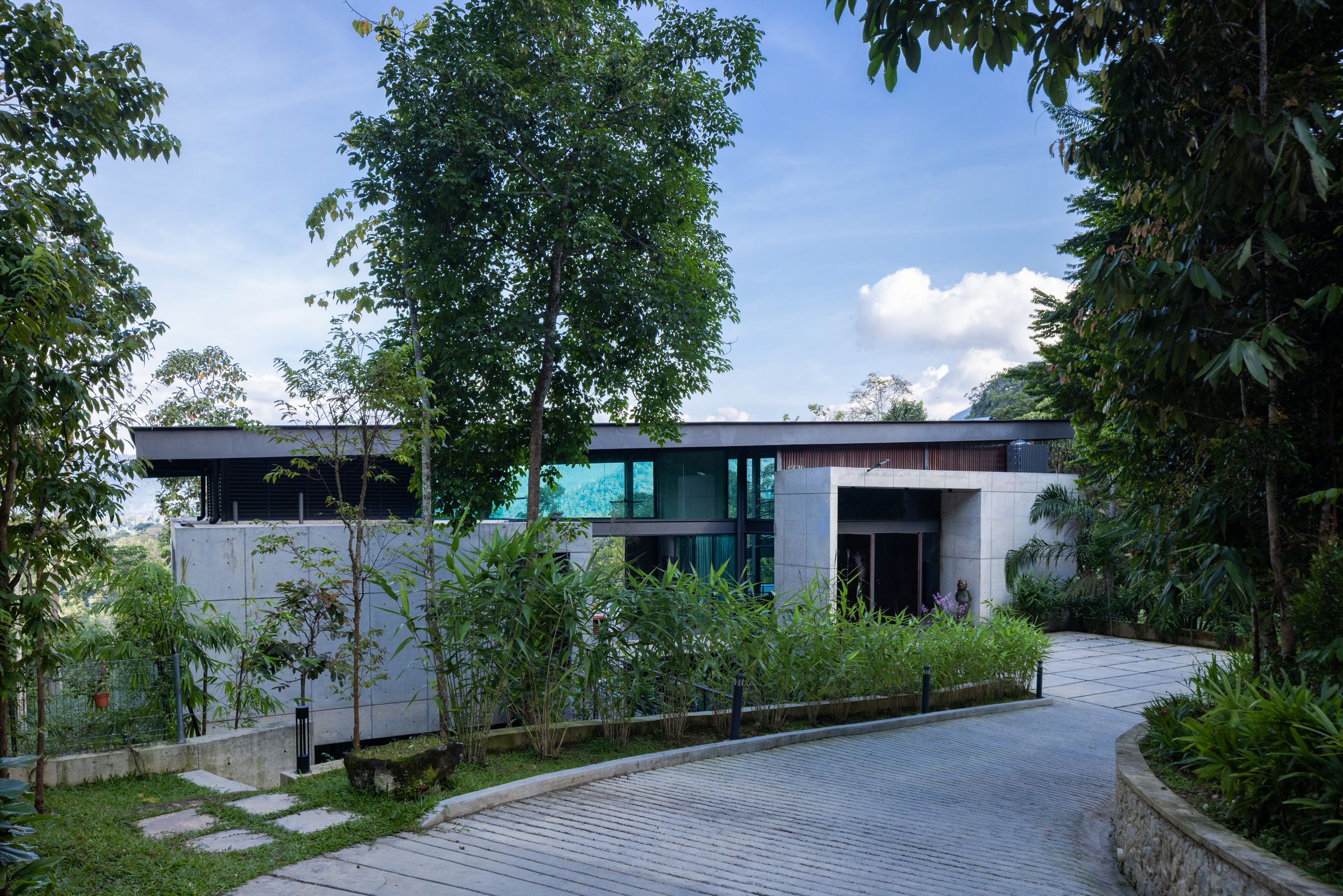 Side view of the SereneNest villa with a concrete garden path through tall trees