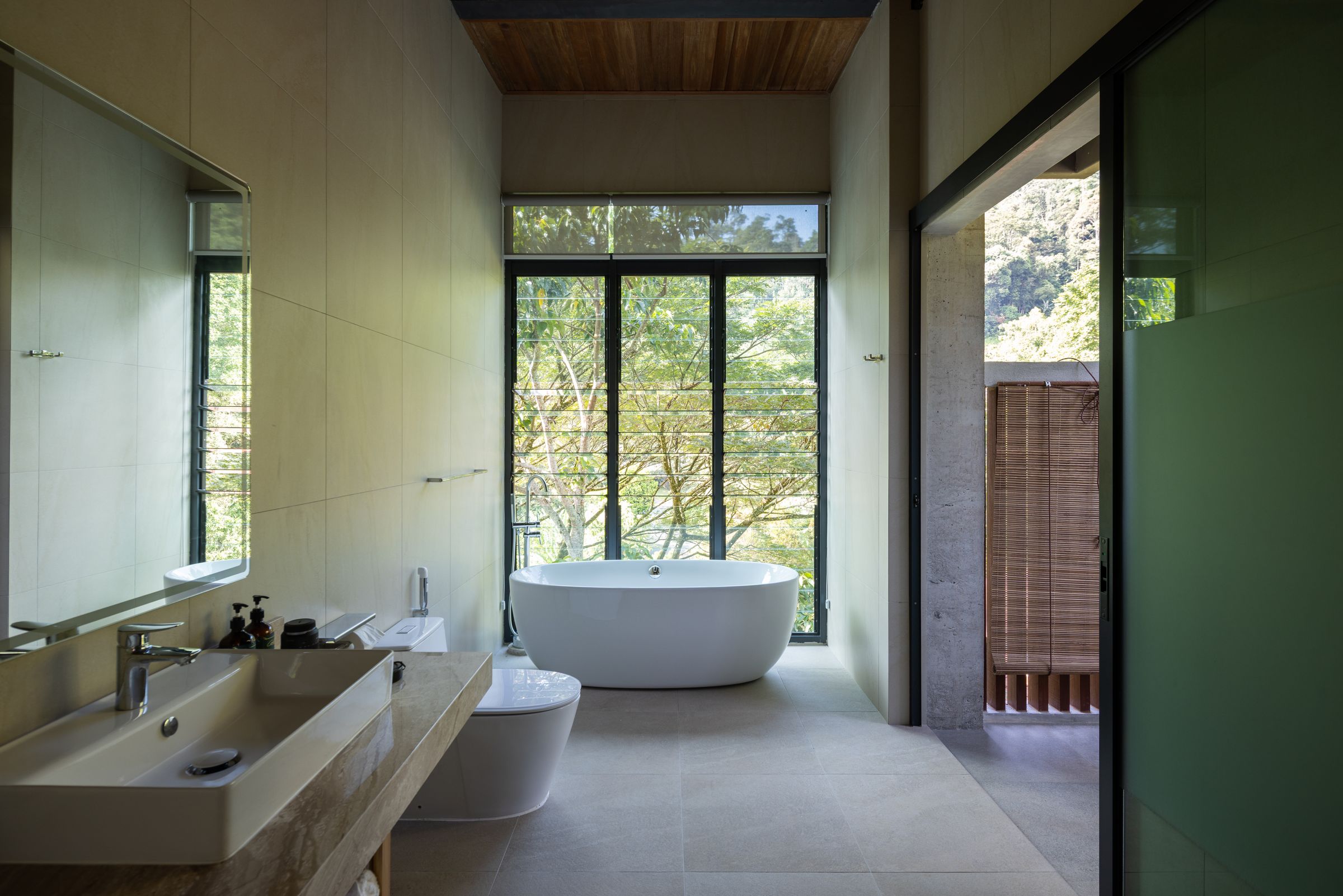 Concrete bathroom at SereneNest with a freestanding tub beside floor-to-ceiling glass