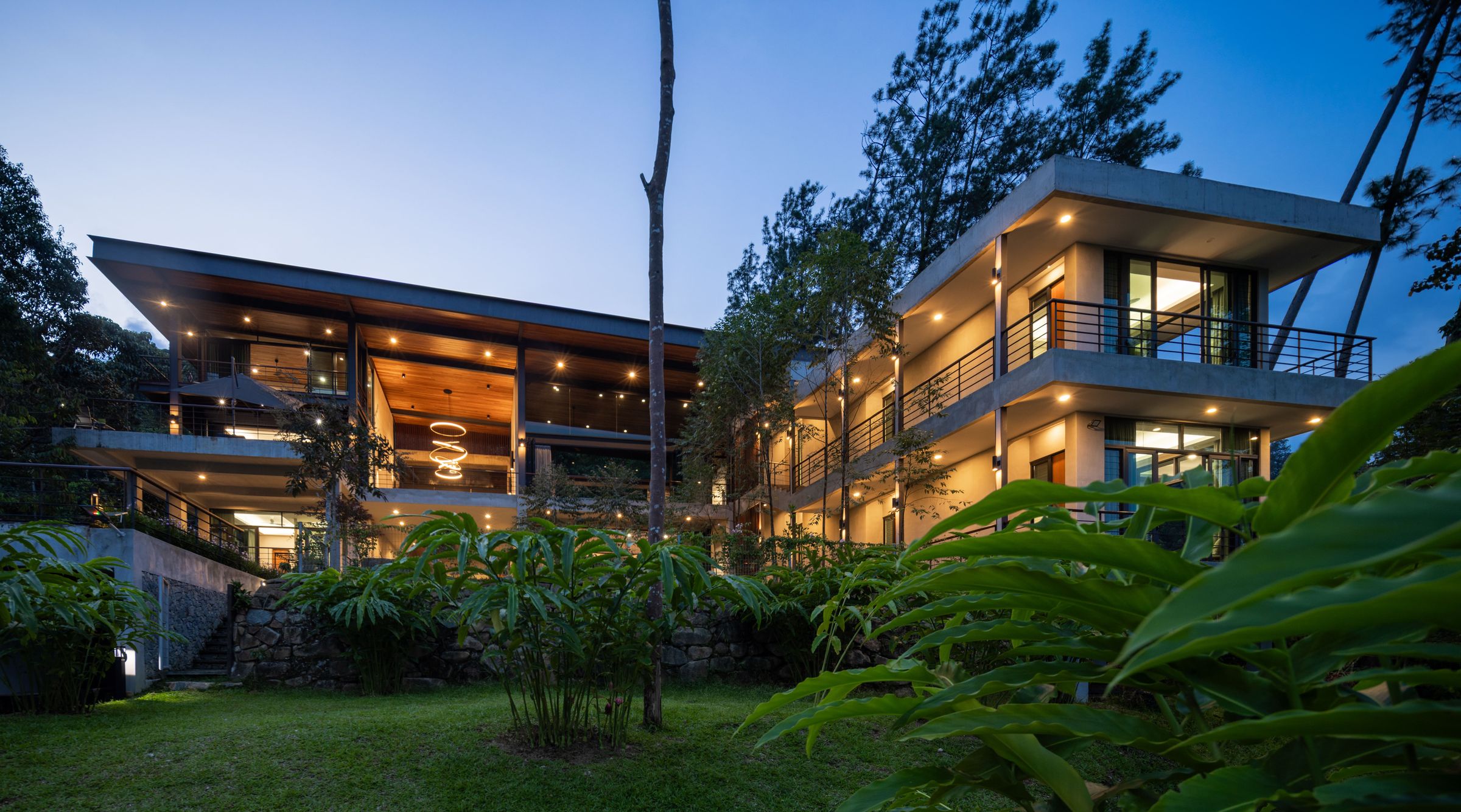 Two-storey SereneNest villa lit at dusk and framed by towering rainforest trees