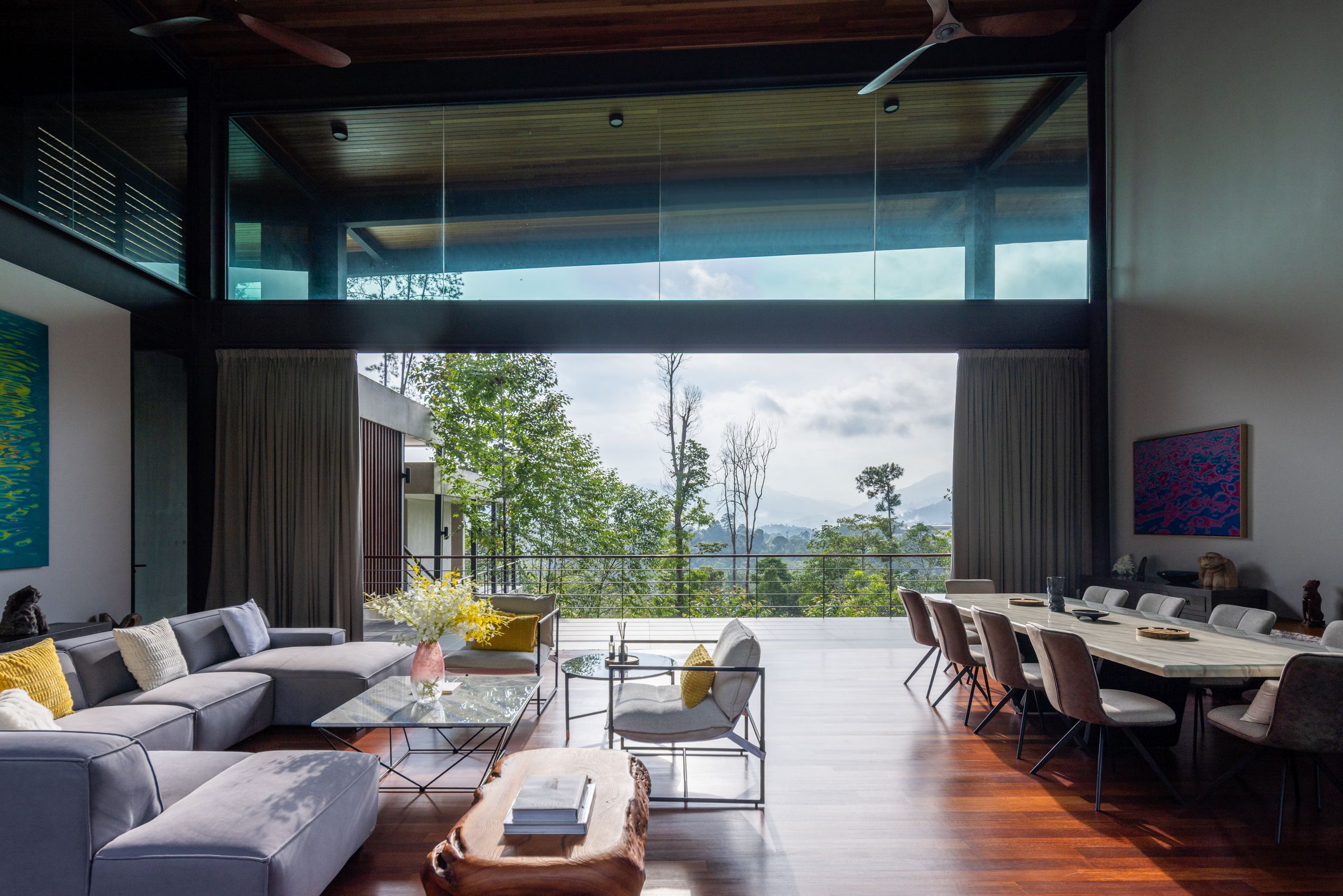 Spacious open lounge and dining at SereneNest with retracted glass walls and a hill view