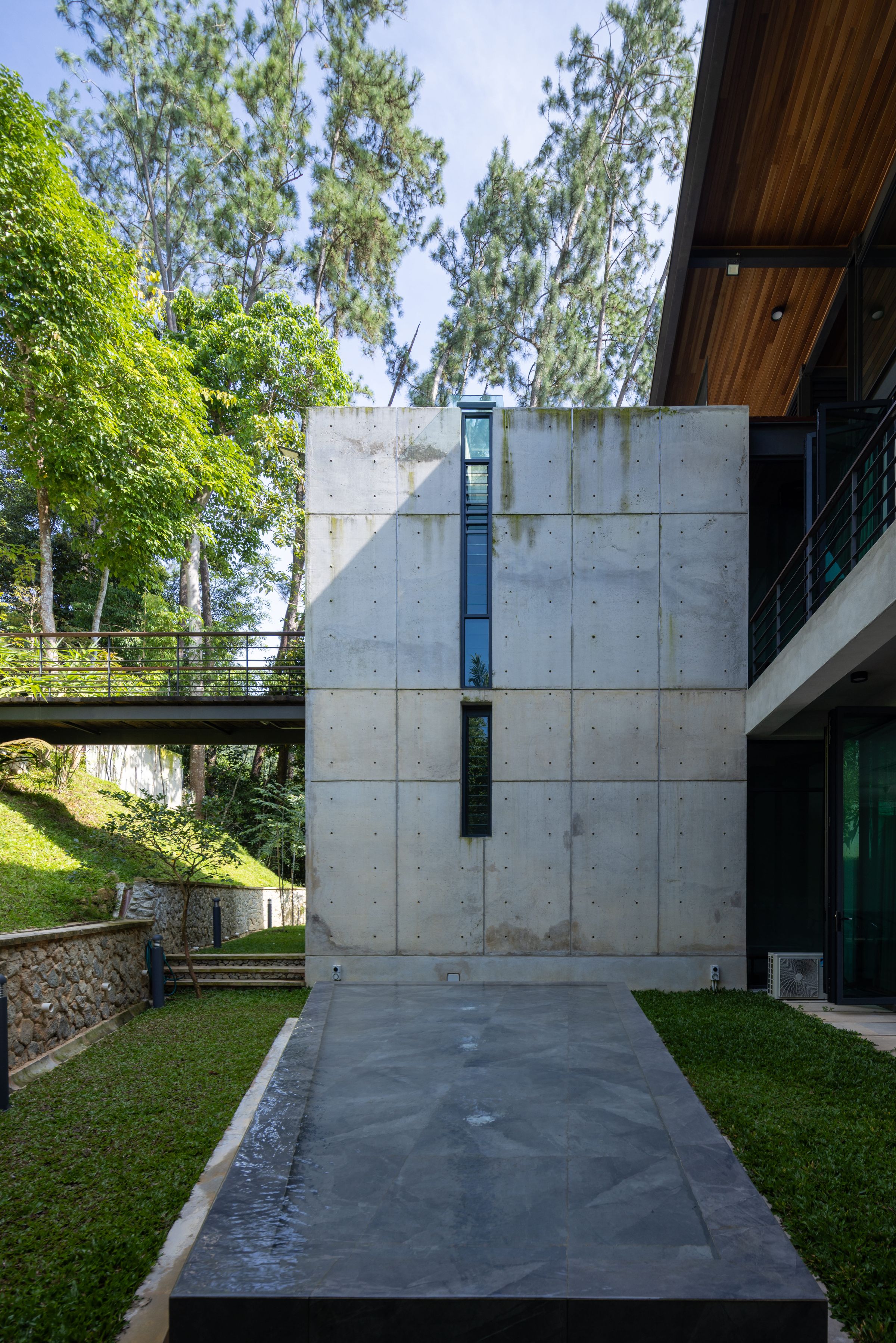 Concrete passage between SereneNest villa wings with a garden courtyard below