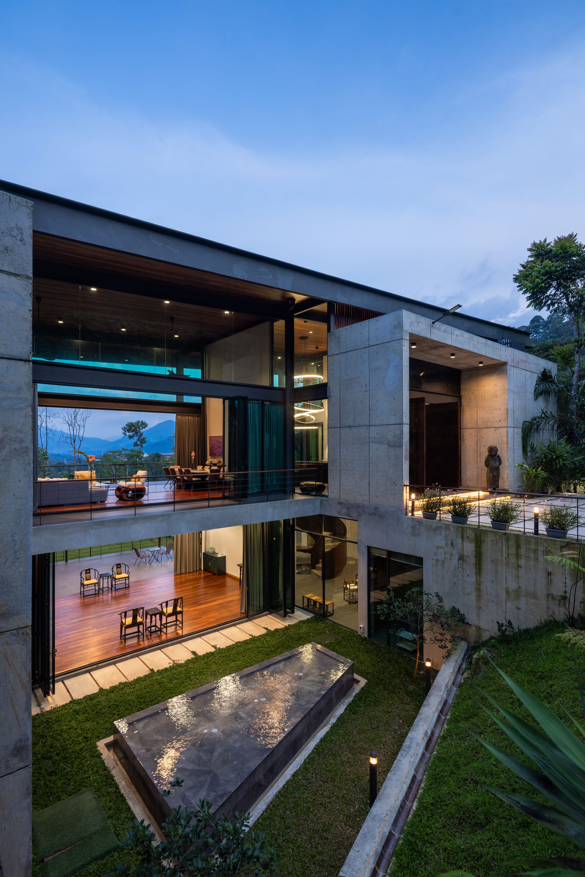 SereneNest villa at dusk with a still reflecting pool catching the warm interior lights