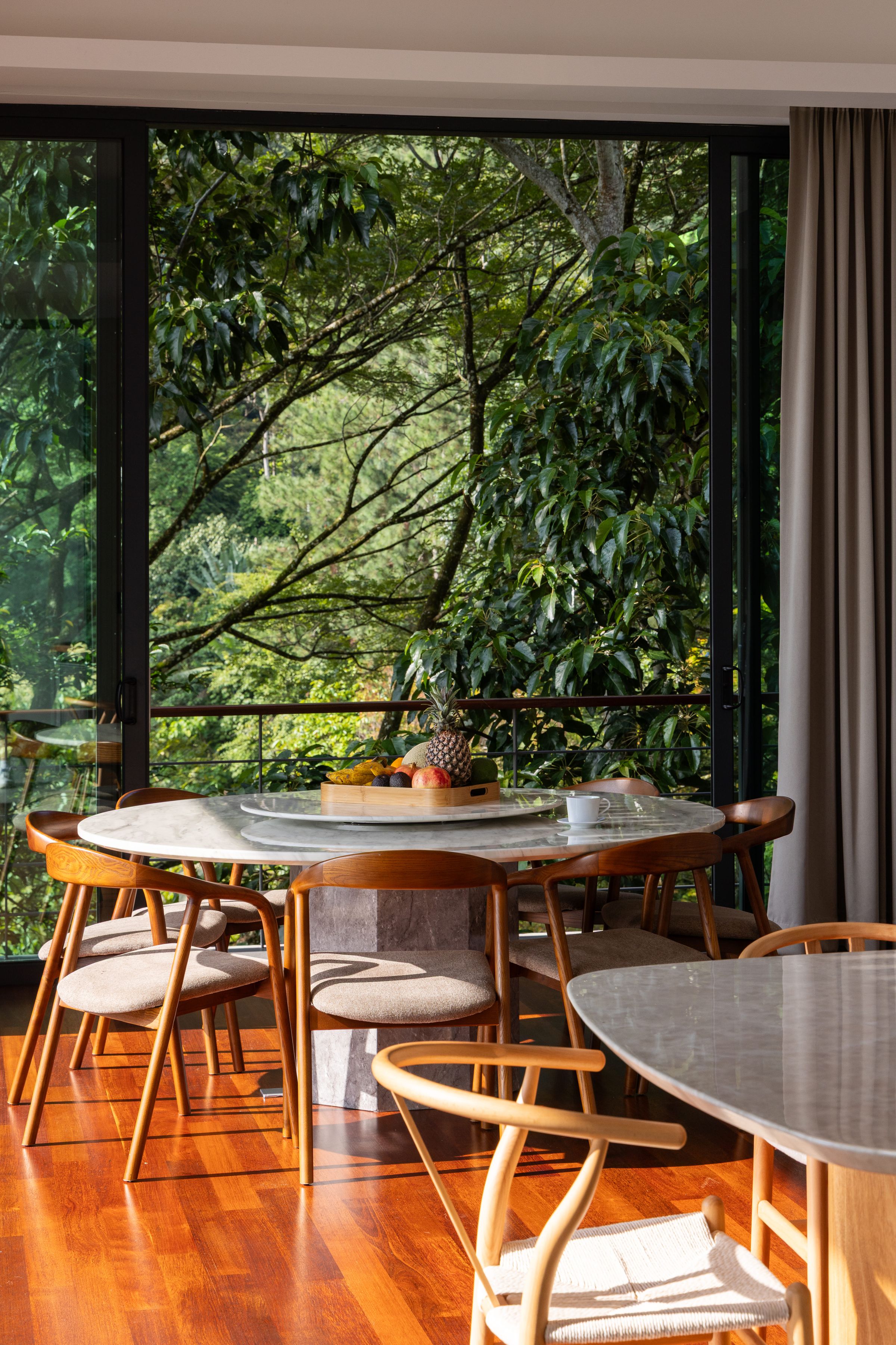 Round timber dining table at SereneNest set beside a tall glass wall onto the forest