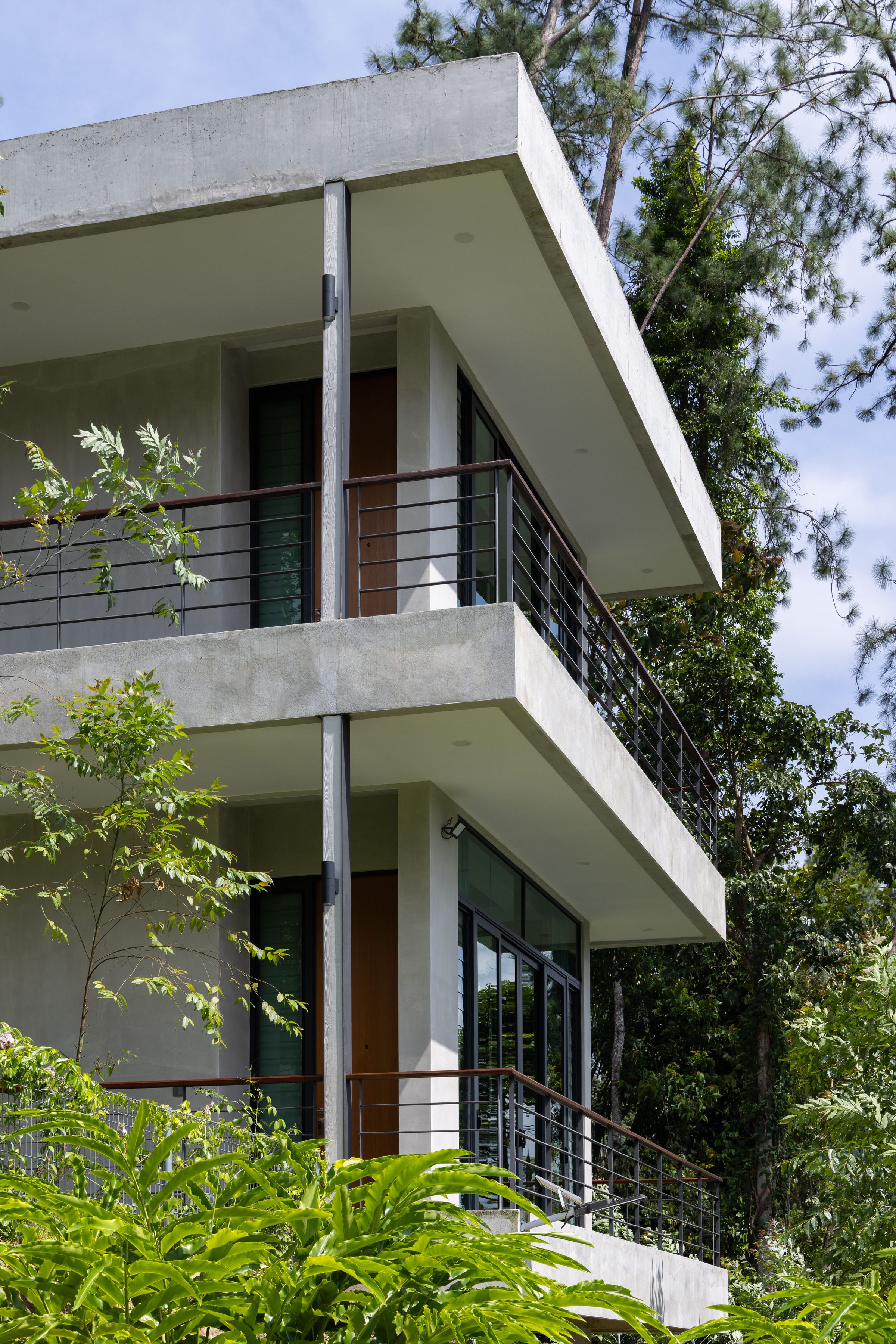 Two-storey concrete and white balcony facade of SereneNest set into thick greenery