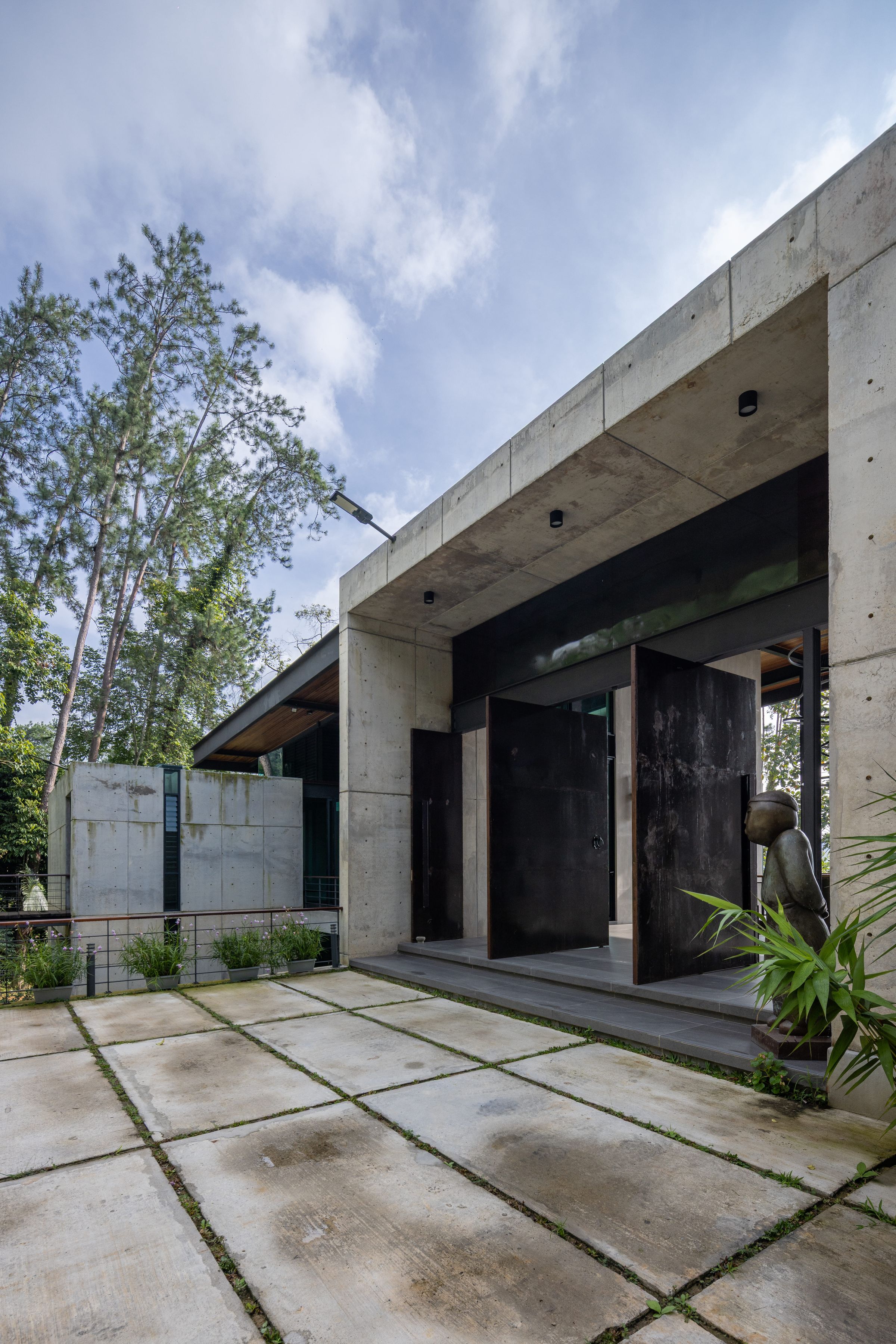 Raw concrete villa entrance at SereneNest with tall trees and a paved approach