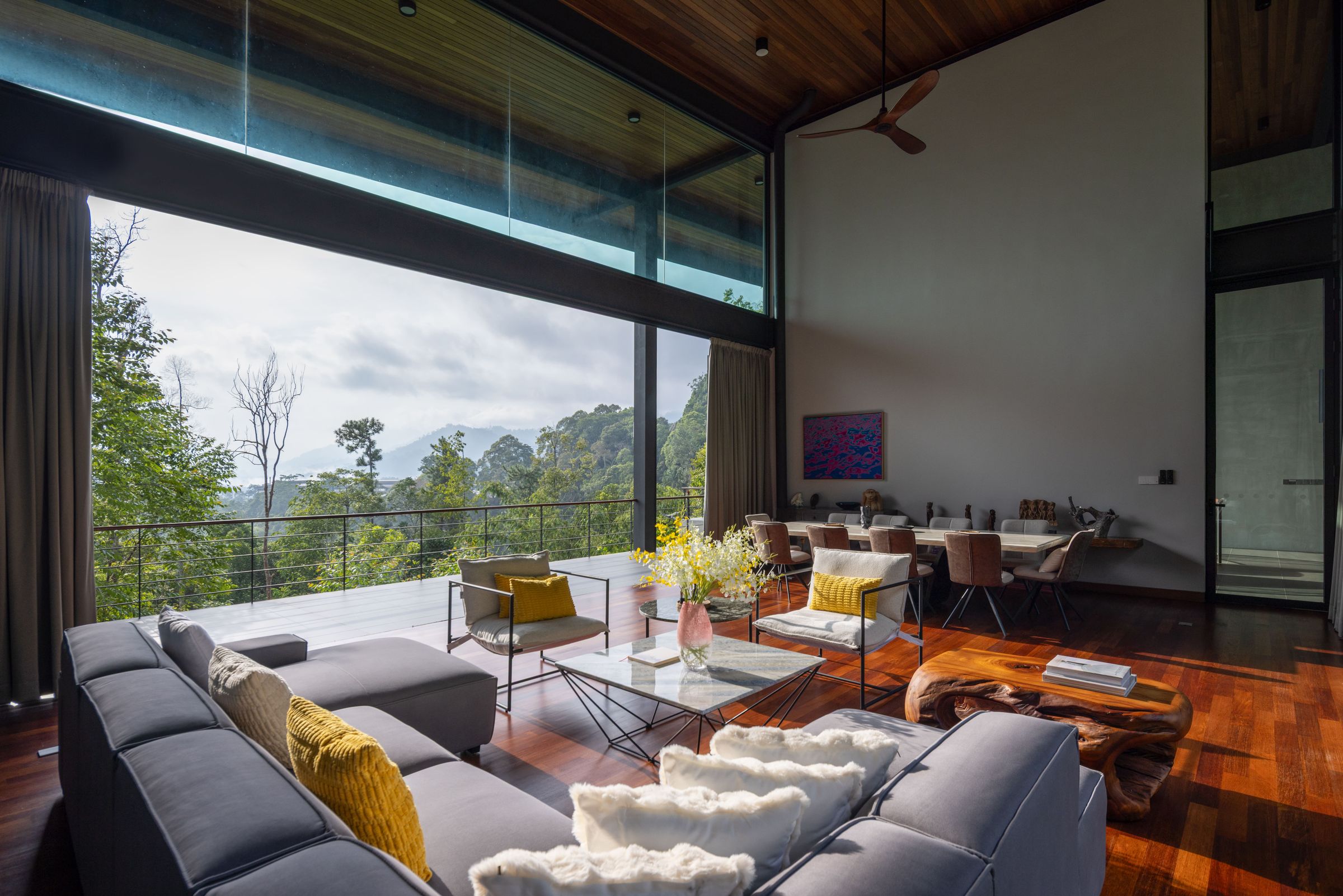Living room at SereneNest with sofas, dining beyond and tall glass onto the forest hills