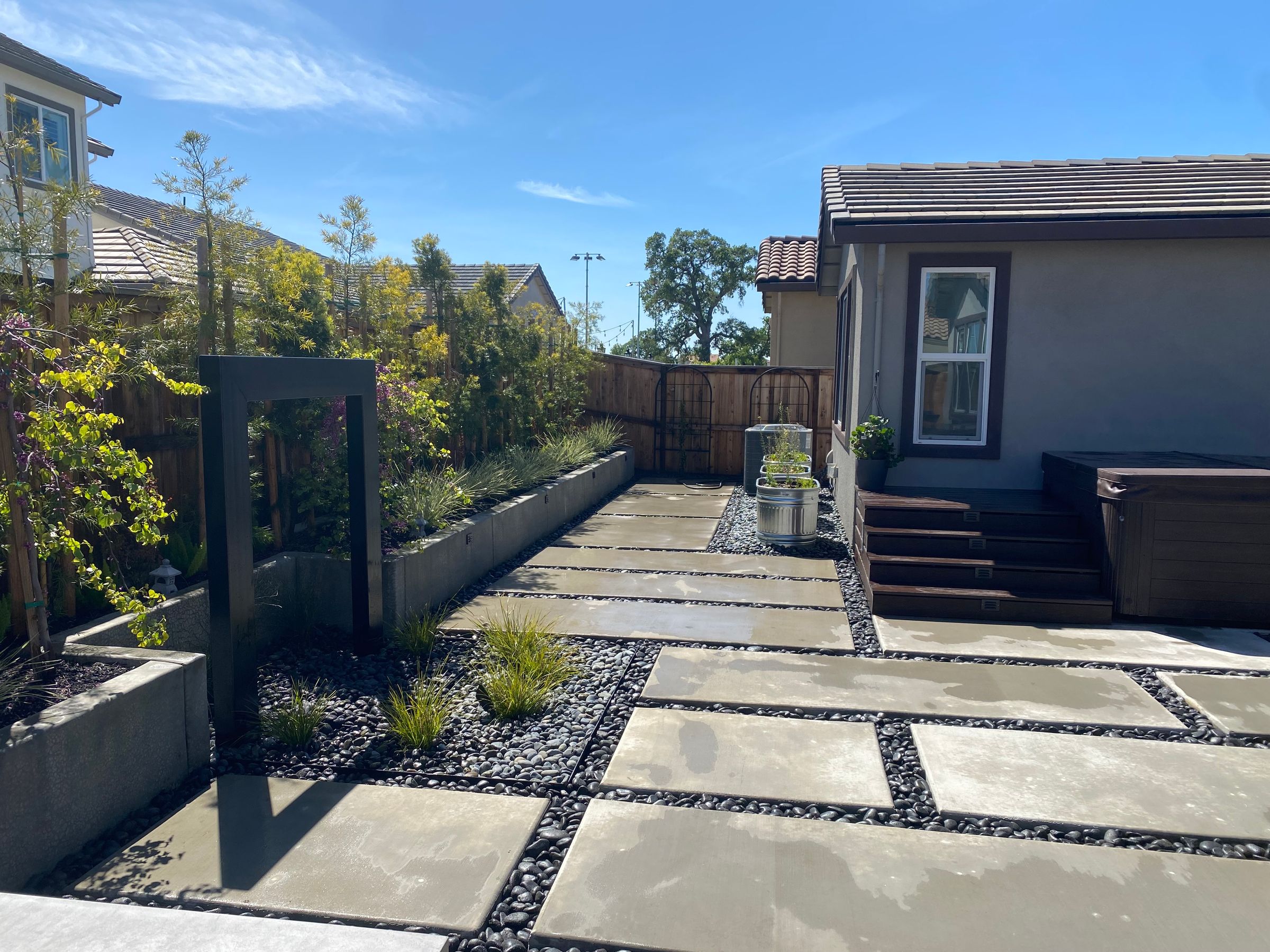 WATER FEATURE, CONCRETE PATIO WITH MEXICAN BEACH PEBBLE, VEGETABLE METAL PLANTERS, DECK